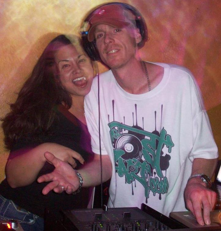 DJ Natural Nate® at the decks with a fan under warm club lighting
